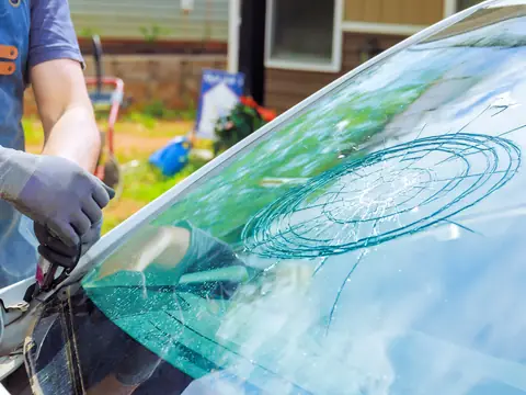 A technician cutting out a shattered windshield on a car parked in a driveway