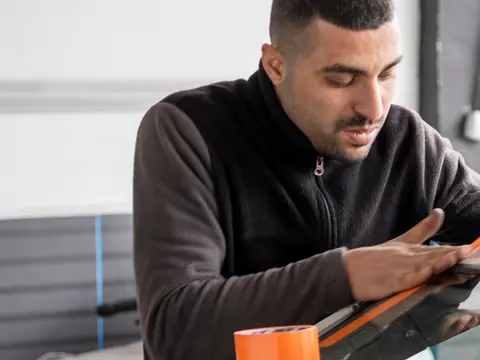 A technician pressing a new windshield into place, with blue suction cup handles on the glass