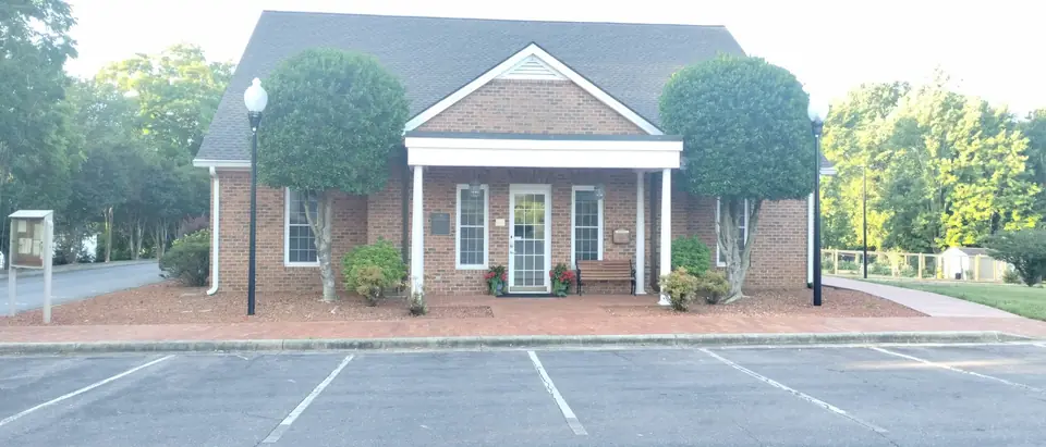 The brick Clemmons Village Hall with white columns, framed by green trees, in Clemmons, NC