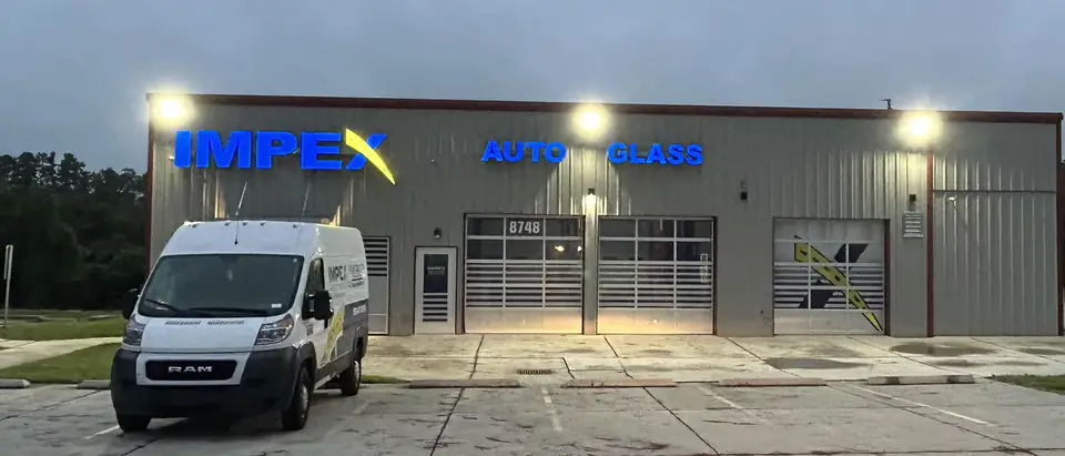 The Impex Auto Glass shop on West Market Street in Greensboro at dusk, with a service van out front
