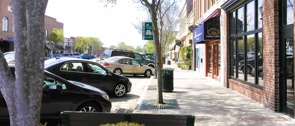 A sidewalk of brick storefronts and young trees in downtown Fuquay-Varina, NC