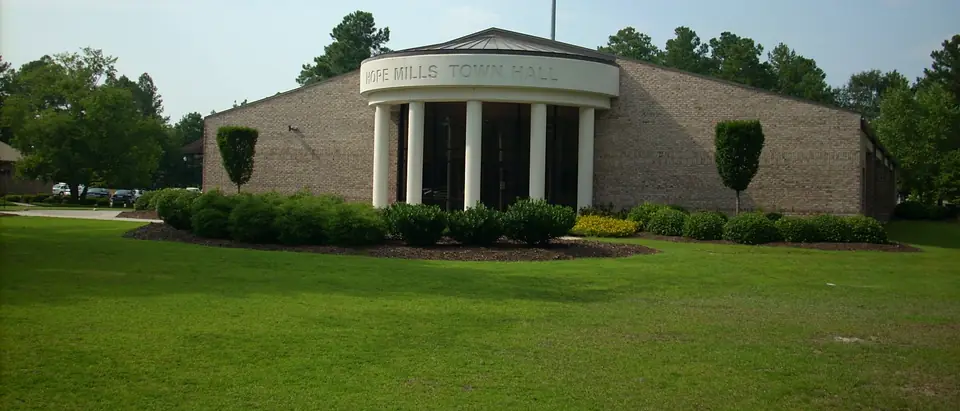 The Hope Mills Town Hall with white columns behind a green lawn in Hope Mills, NC