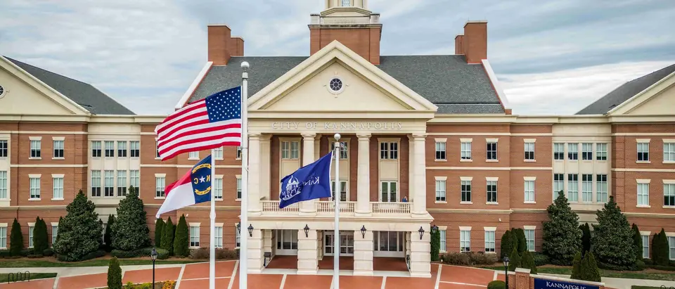 Kannapolis City Hall with its white clock cupola behind flags and a brick plaza in Kannapolis, NC