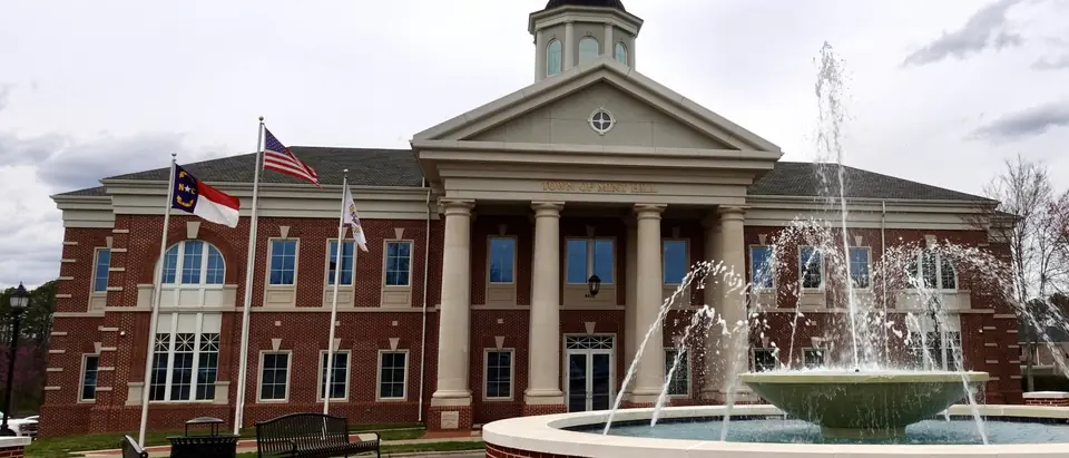 Mint Hill Town Hall, a red-brick building with white columns behind a splashing fountain in Mint Hill, NC