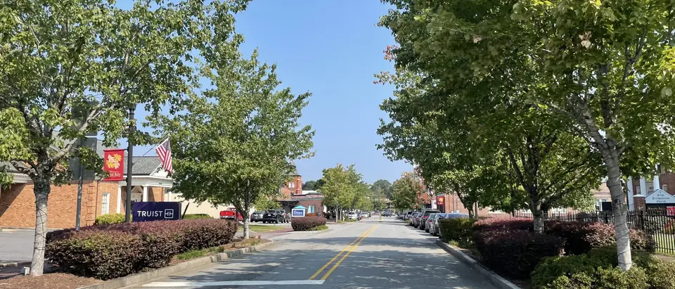 A tree-lined street through downtown Mount Holly, NC, under a clear blue sky