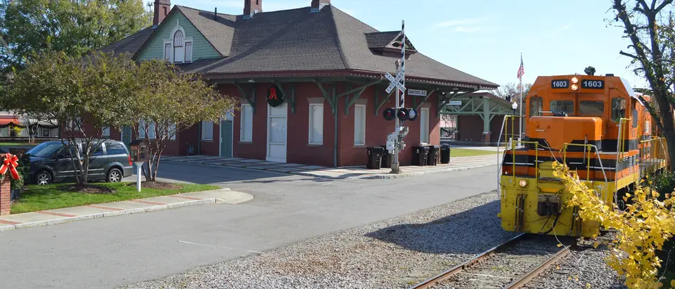 The historic Sanford railroad depot with an orange locomotive beside it in Sanford, NC