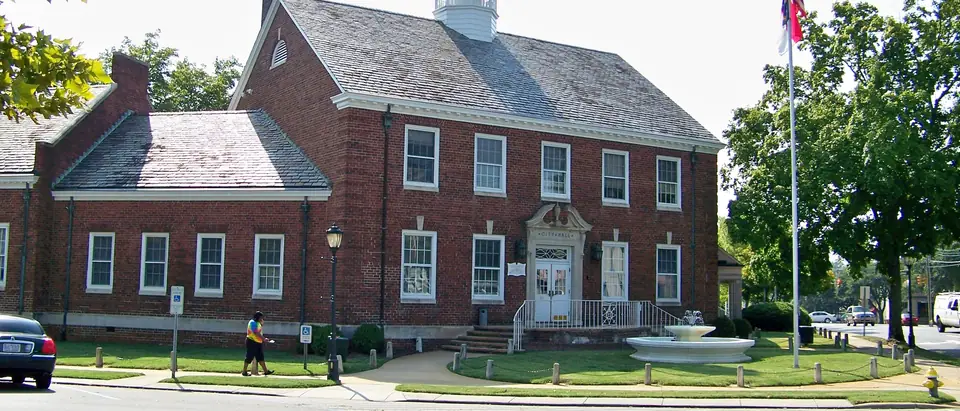 The red-brick Shelby City Hall with its white cupola and a fountain on the lawn in Shelby, NC
