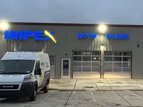 The Impex Auto Glass shop on West Market Street in Greensboro at dusk, with a service van out front