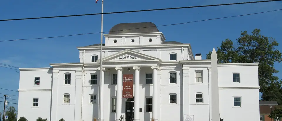 The white Old Wilkes County Courthouse with flowers and a flagpole under a deep blue sky in Wilkesboro, NC